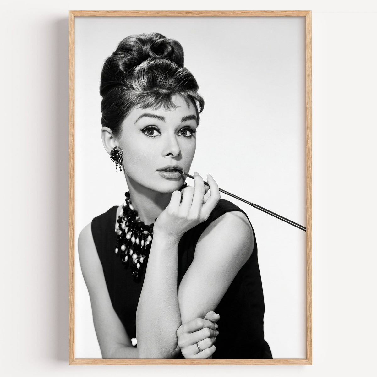 Woman with updo, pearls and long cigarette holder print in a light oak frame on a plain white wall