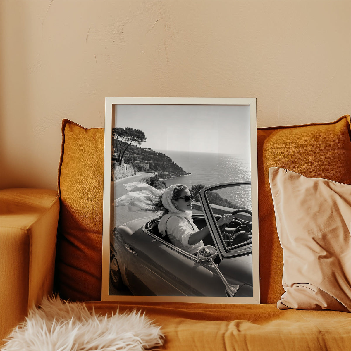 Woman driving a convertible with flowing scarf print in a white frame leaning on a mustard velvet sofa