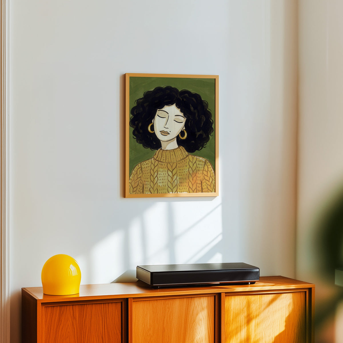 Olive and mustard portrait print in a light oak frame above a teak sideboard with a yellow lamp