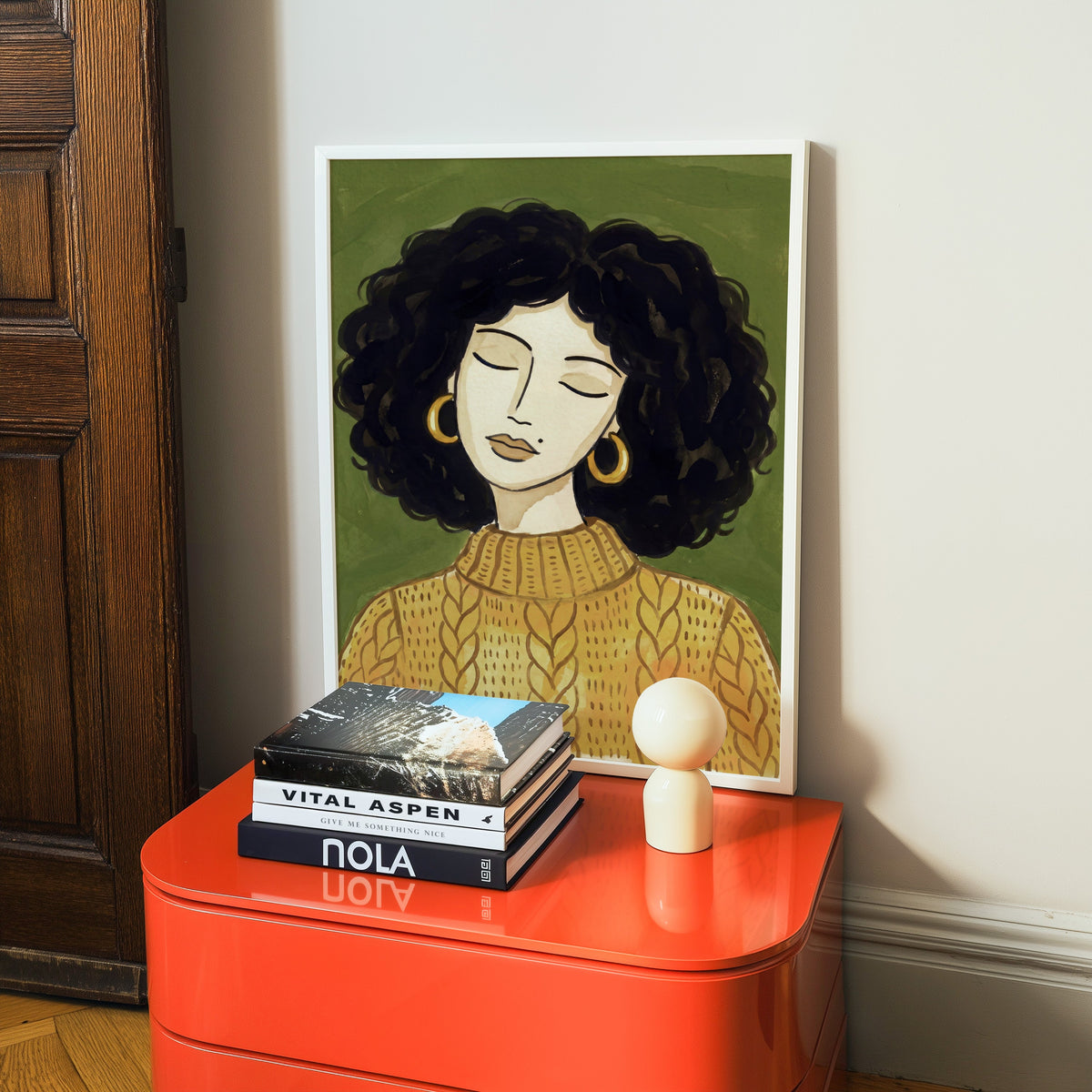 Line art woman portrait print in a white frame on a glossy orange cabinet with books