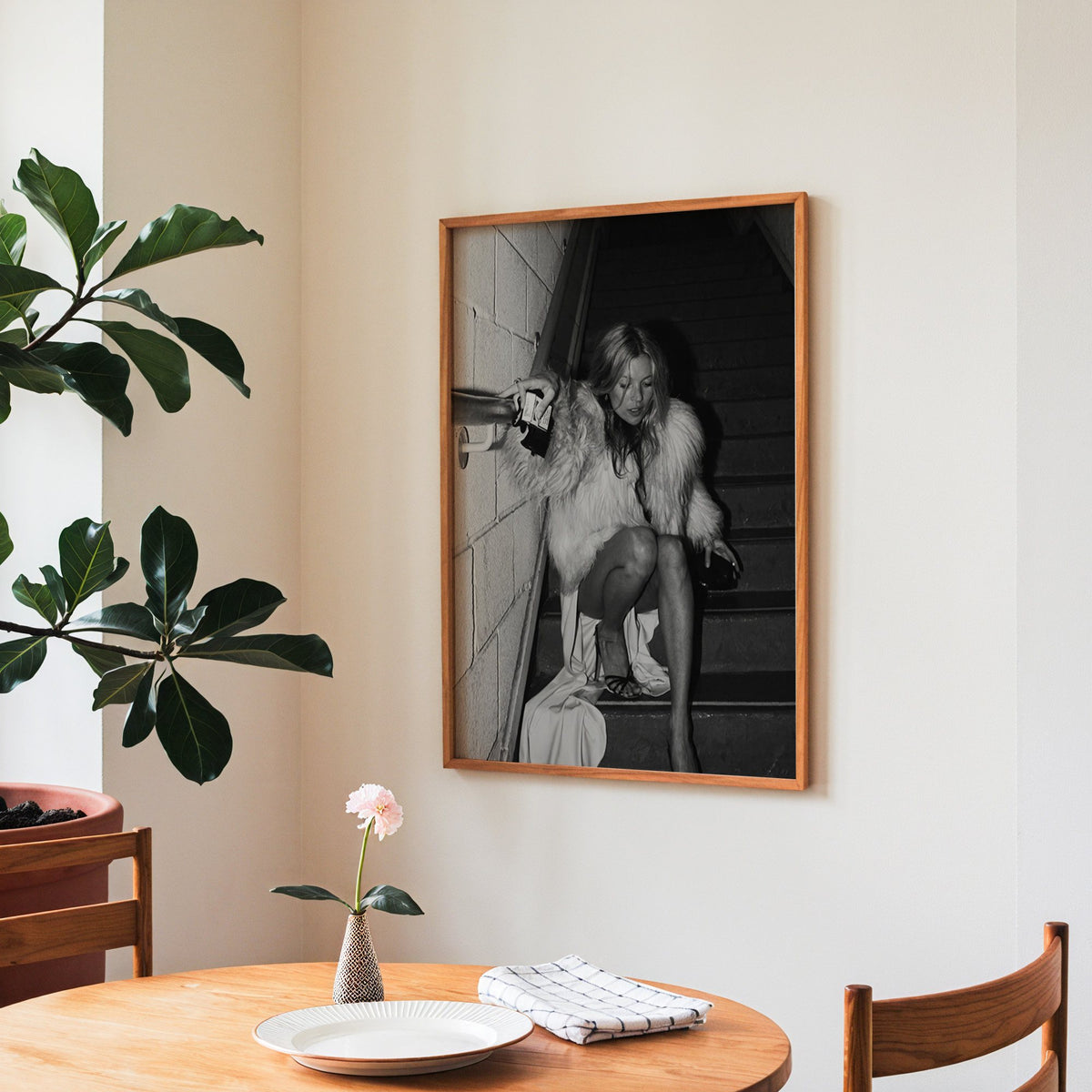 Woman in shaggy fur coat crouched on stairs print in a teak frame above a round wooden dining table