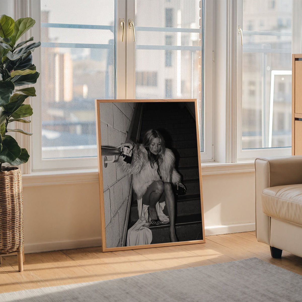 Woman in shaggy fur coat crouched on stairs print in an oak frame leaning on the floor beside a fiddle leaf fig