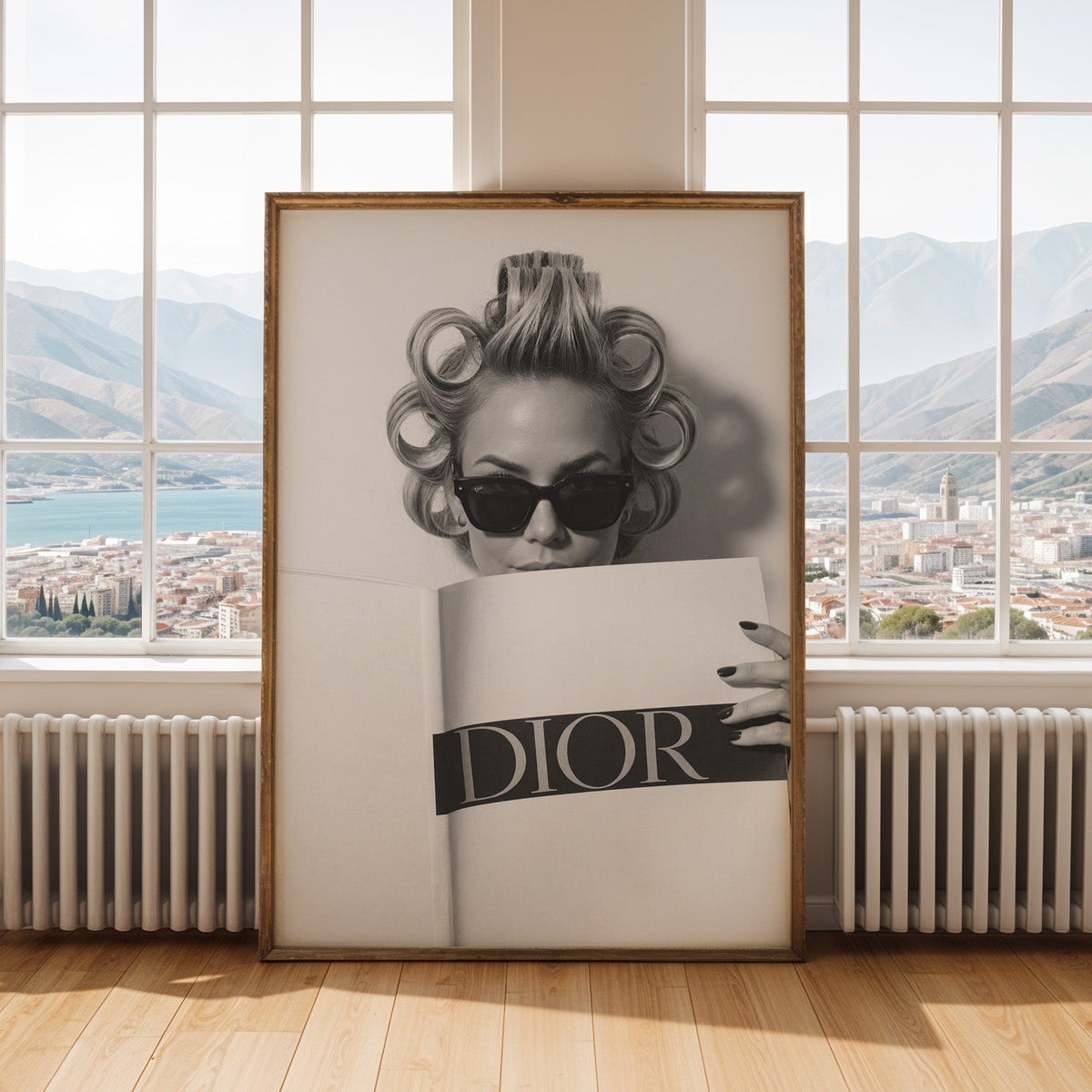 Woman in hair rollers and sunglasses behind magazine print shown in an antique gold frame by tall windows with a sea view