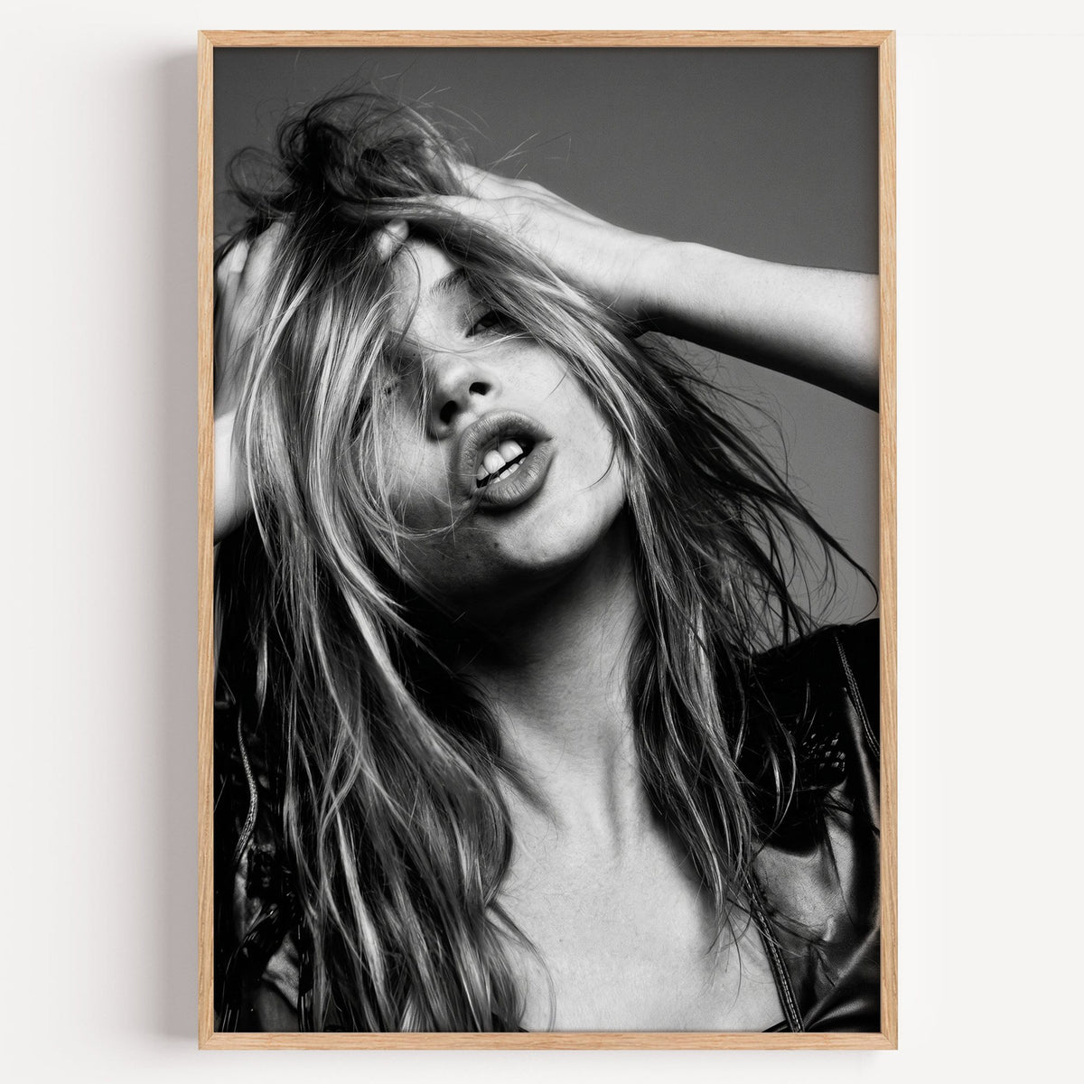 Woman pushing hands through messy hair print in a light oak frame on a plain white wall