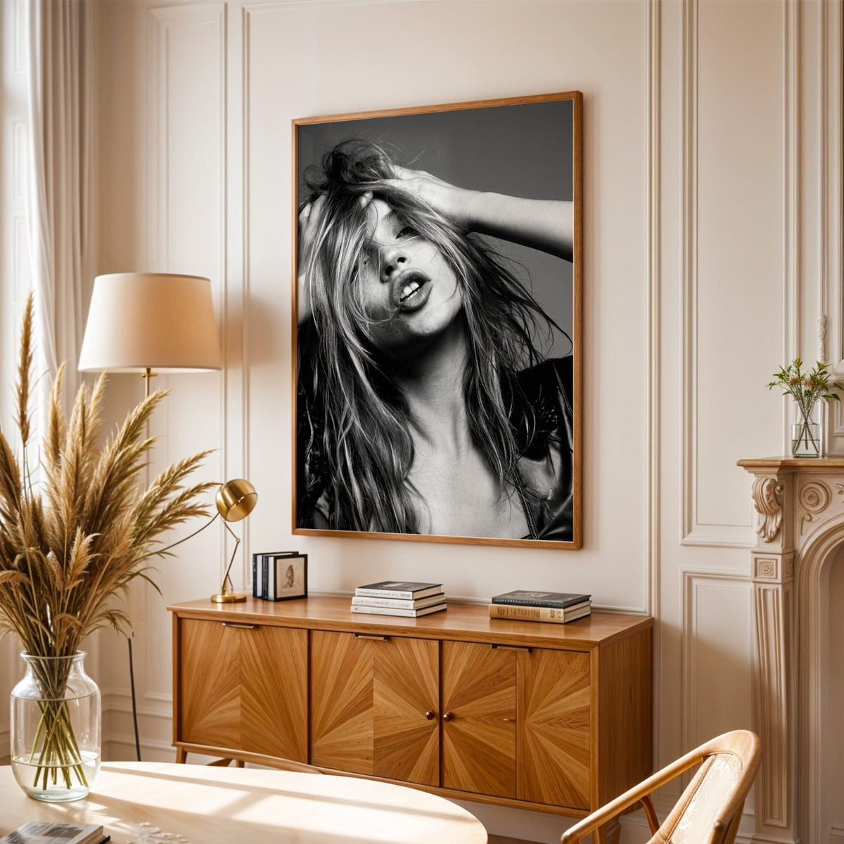Woman pushing hands through messy hair print in an oak frame above a sunburst wood sideboard with pampas grass