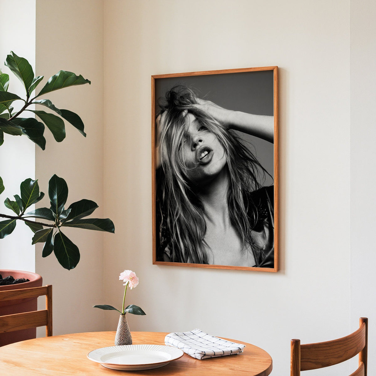 Woman pushing hands through messy hair print in a teak frame above a round wooden dining table