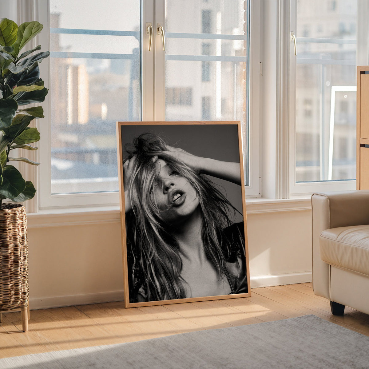Woman pushing hands through messy hair print in an oak frame leaning on the floor beside a fiddle leaf fig