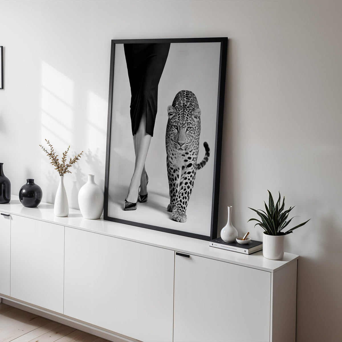 Woman's legs in heels walking beside leopard print in a black frame on a white sideboard with black and white vases