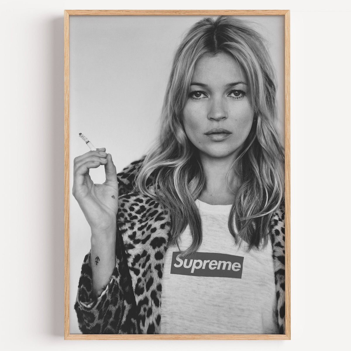 Woman in leopard coat holding a cigarette print in a light oak frame on a plain white wall