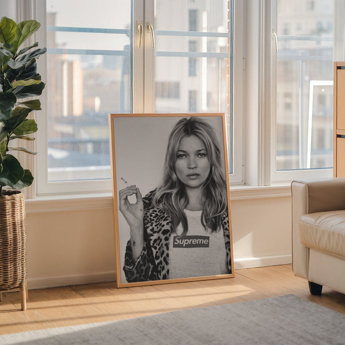 Woman in leopard coat holding a cigarette print in an oak frame leaning on the floor beside a fiddle leaf fig