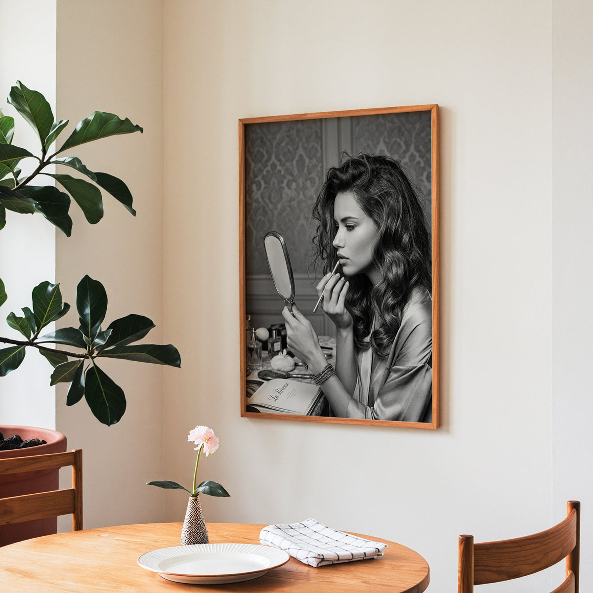 Woman lining lips with silver hand mirror print in a teak frame above a round wooden dining table
