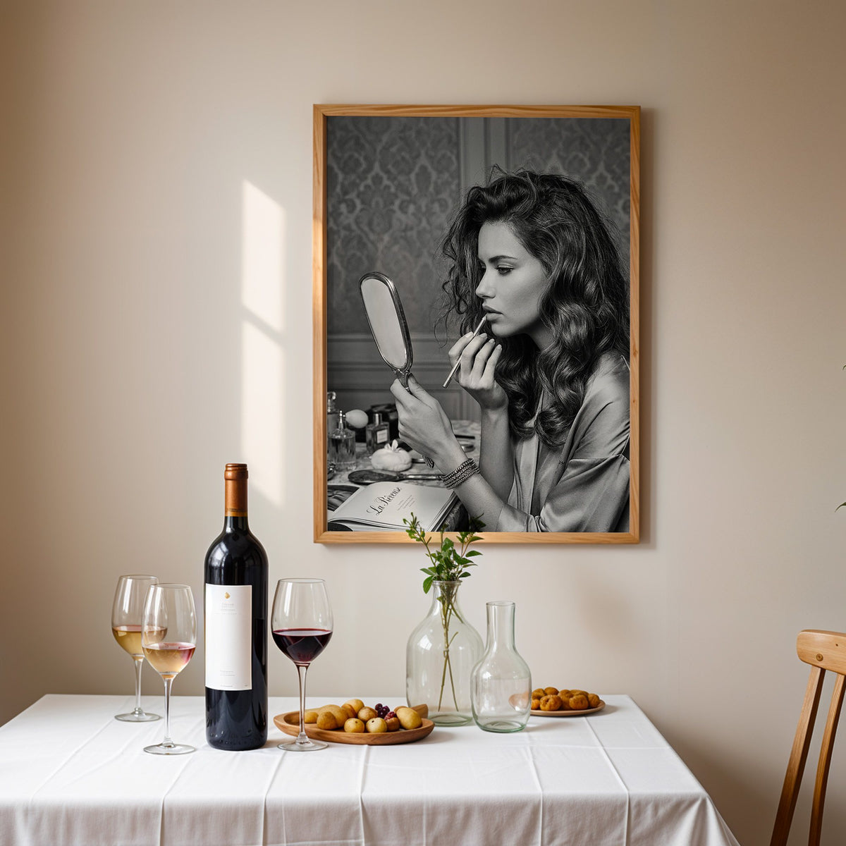 Woman lining lips with silver hand mirror print in an oak frame above a table set with red wine and glasses