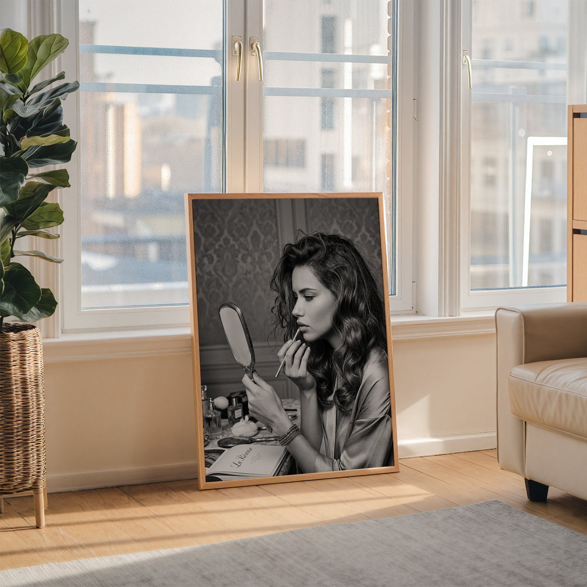 Woman lining lips with silver hand mirror print in an oak frame leaning on the floor beside a fiddle leaf fig