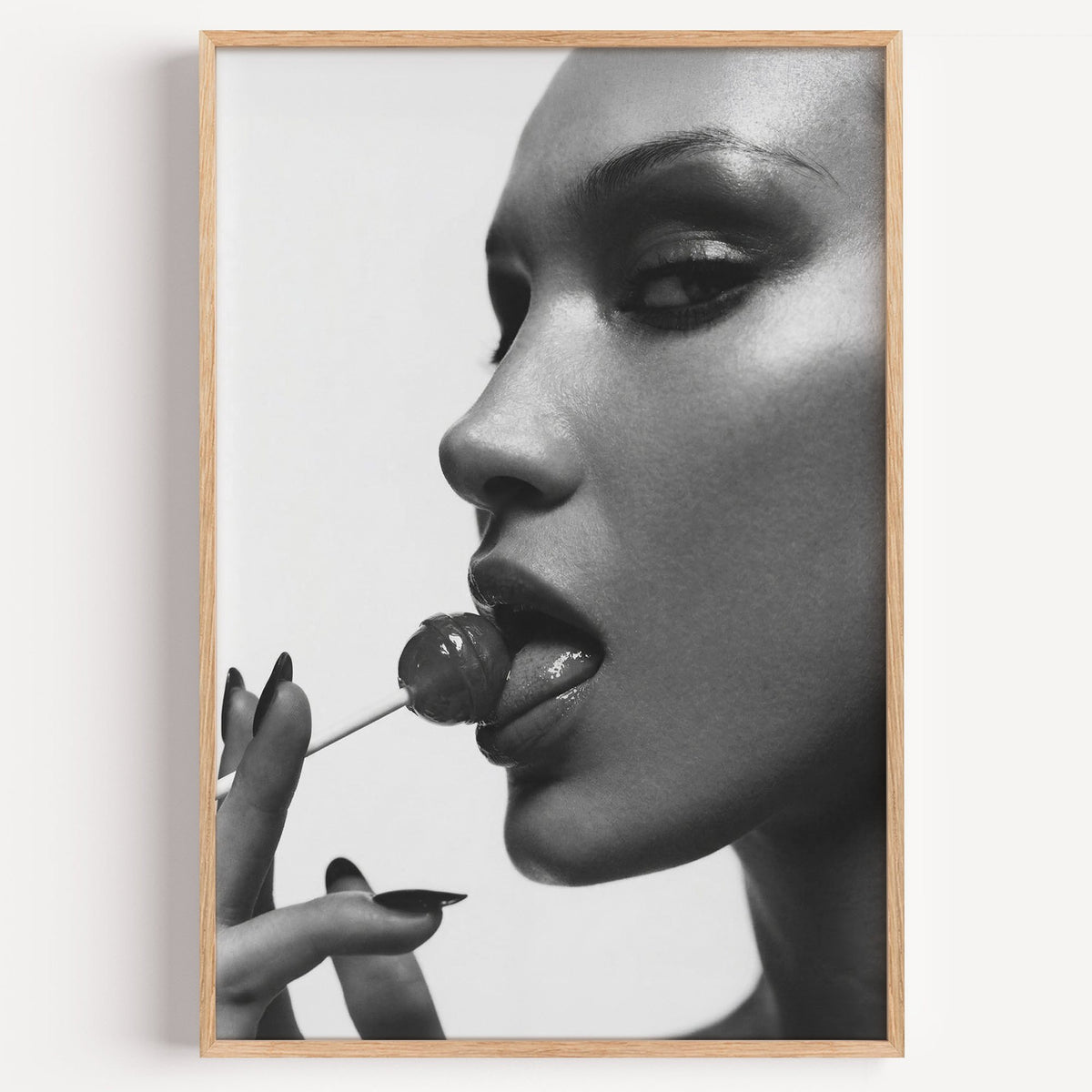 Glossy closeup with lollipop and black nails print in a light oak frame on a plain white wall