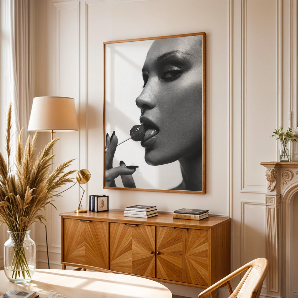 Glossy closeup with lollipop and black nails print in an oak frame above a sunburst wood sideboard with pampas grass