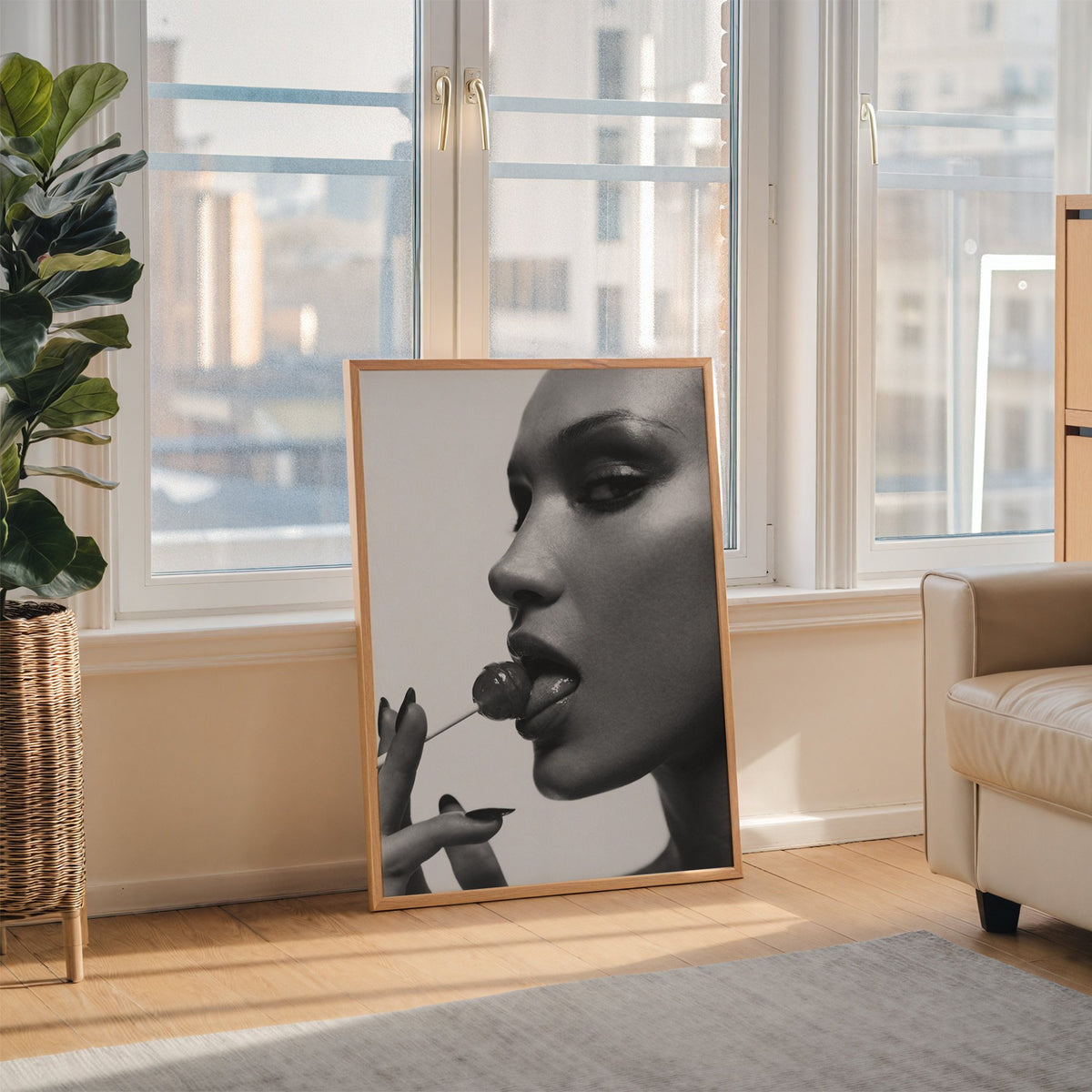 Glossy closeup with lollipop and black nails print in an oak frame leaning on the floor beside a fiddle leaf fig