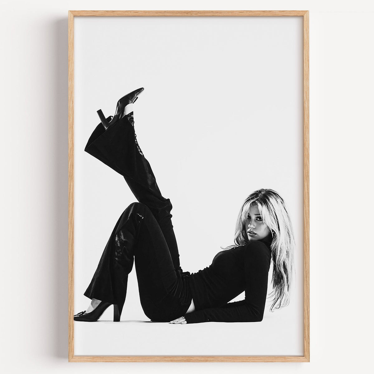 Woman in all black lying with leg raised print in a light oak frame on a plain white wall