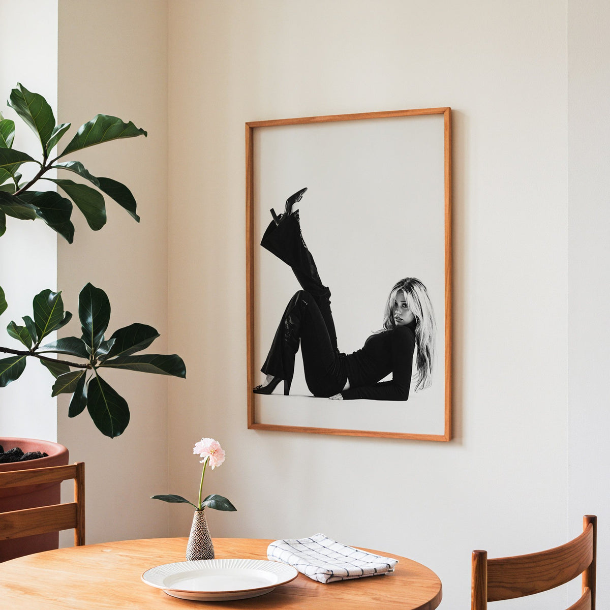 Woman in all black lying with leg raised print in a teak frame above a round wooden dining table