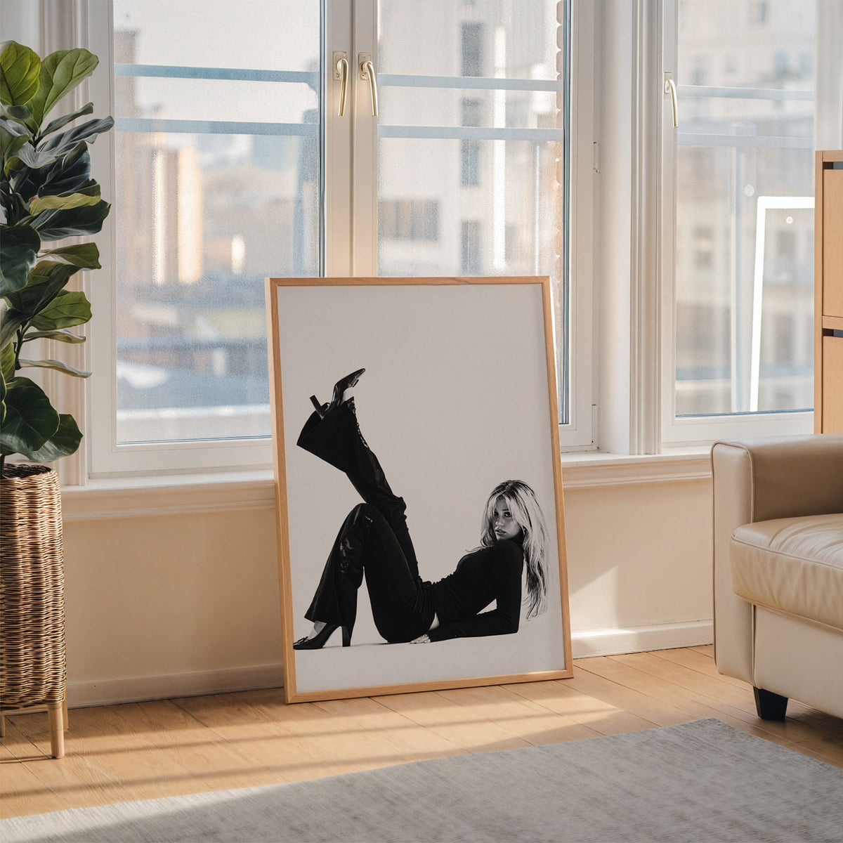 Woman in all black lying with leg raised print in an oak frame leaning on the floor beside a fiddle leaf fig