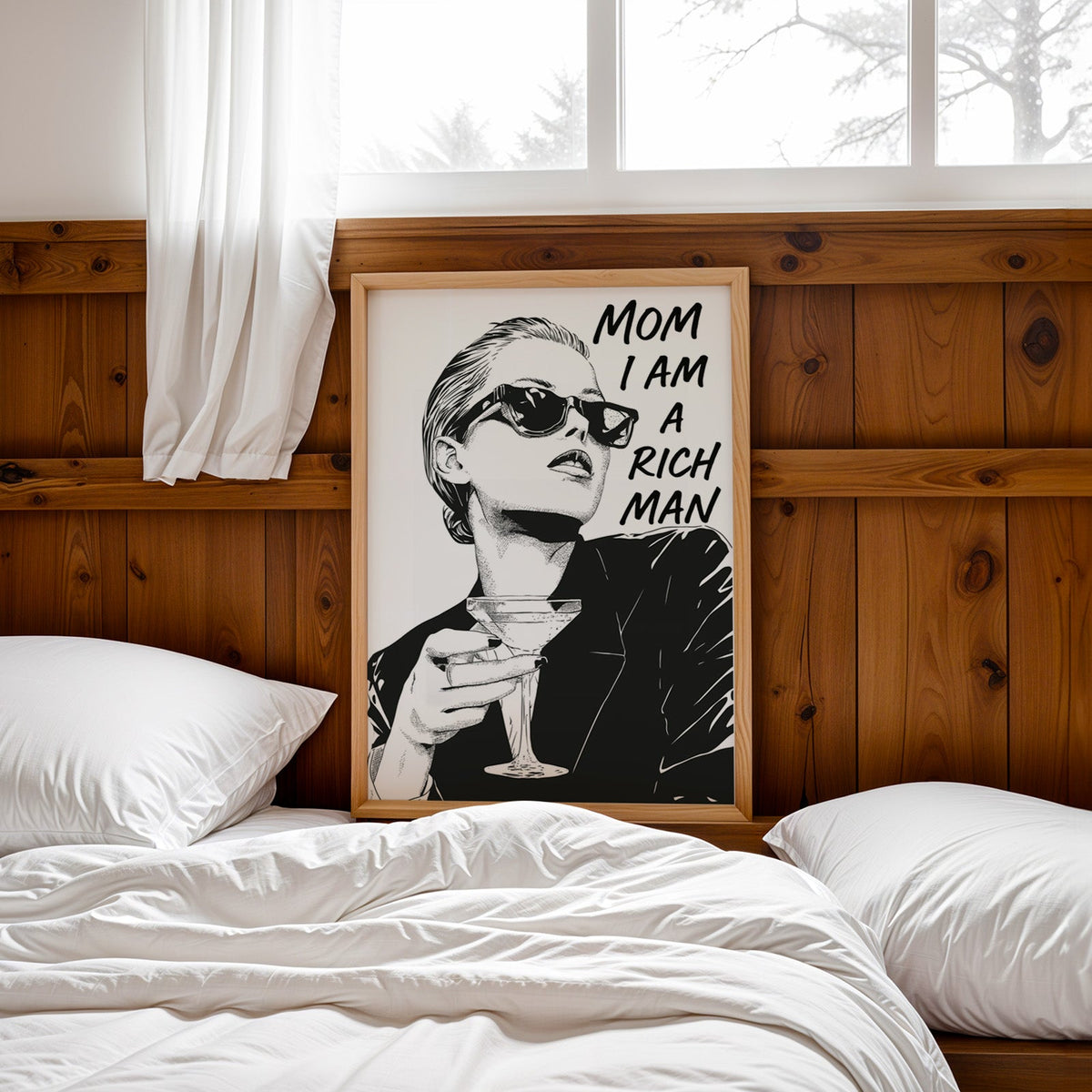Woman in sunglasses with martini ink print in a pine frame leaning on a wood headboard over white bedding