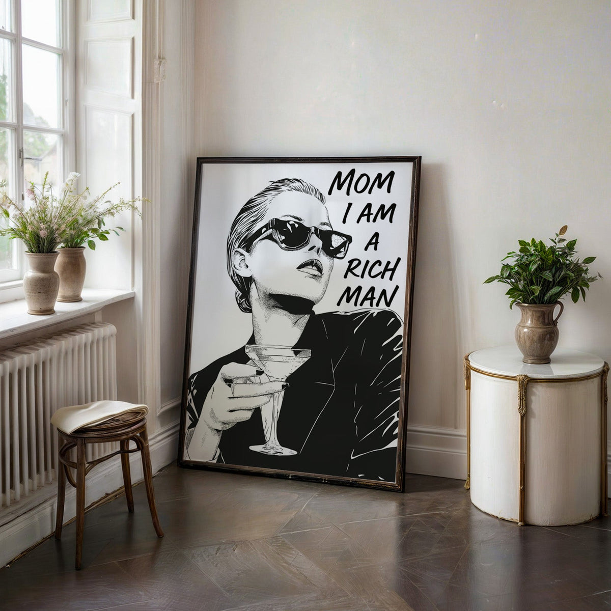 Woman in sunglasses with martini ink print in a black frame on a dark stone floor beside a white side table