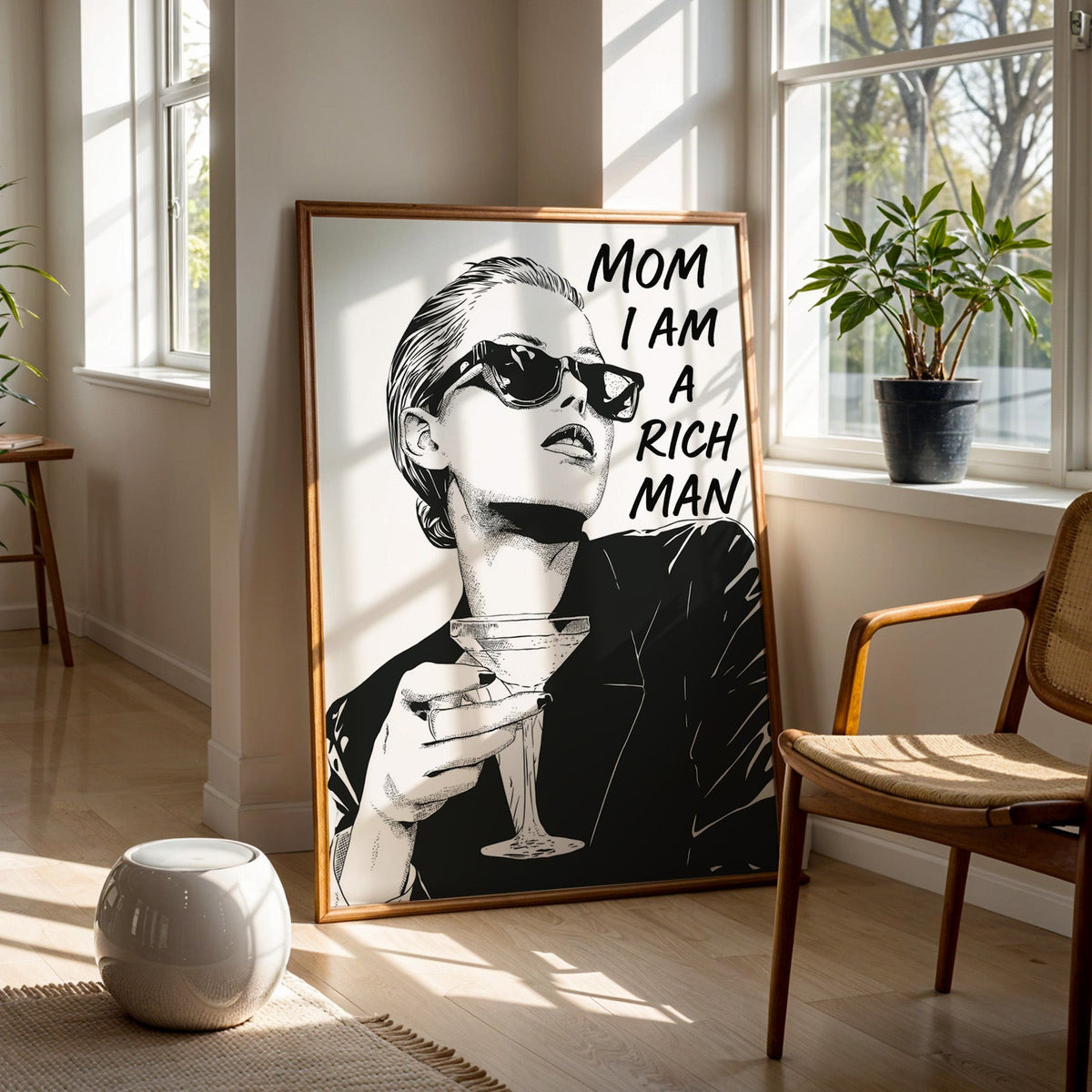 Woman in sunglasses with martini ink print in a walnut frame on a wood floor beside a cane chair and sunny window