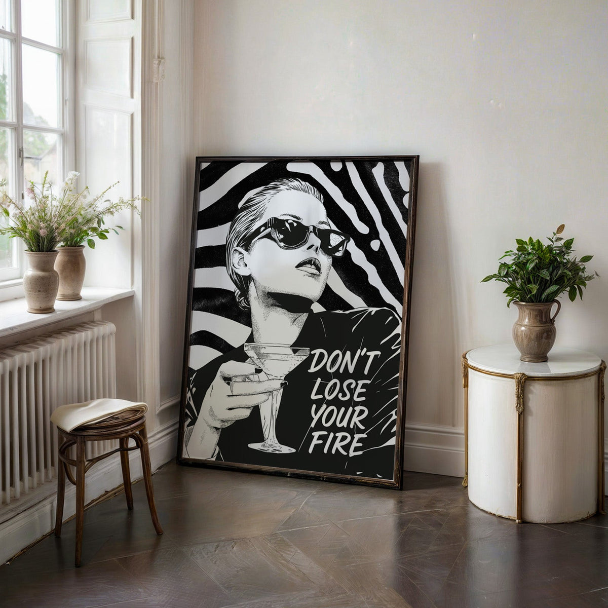Woman with martini on zebra stripe backdrop ink print in a black frame on a dark stone floor beside a white side table