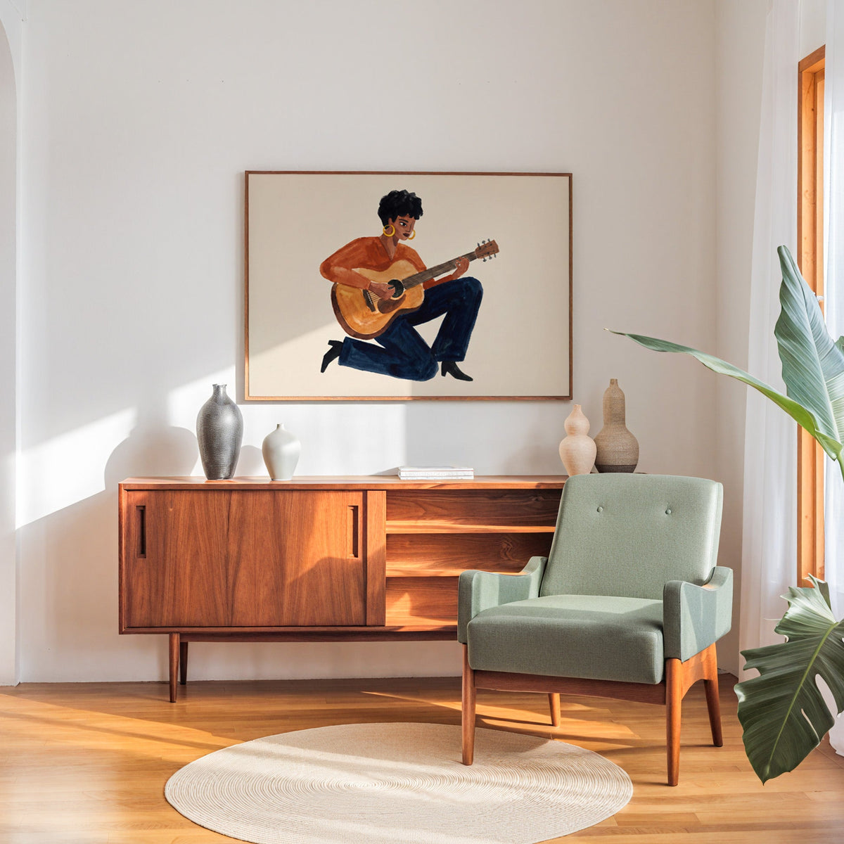Rust and navy guitar print in a walnut frame above a sideboard beside a sage armchair