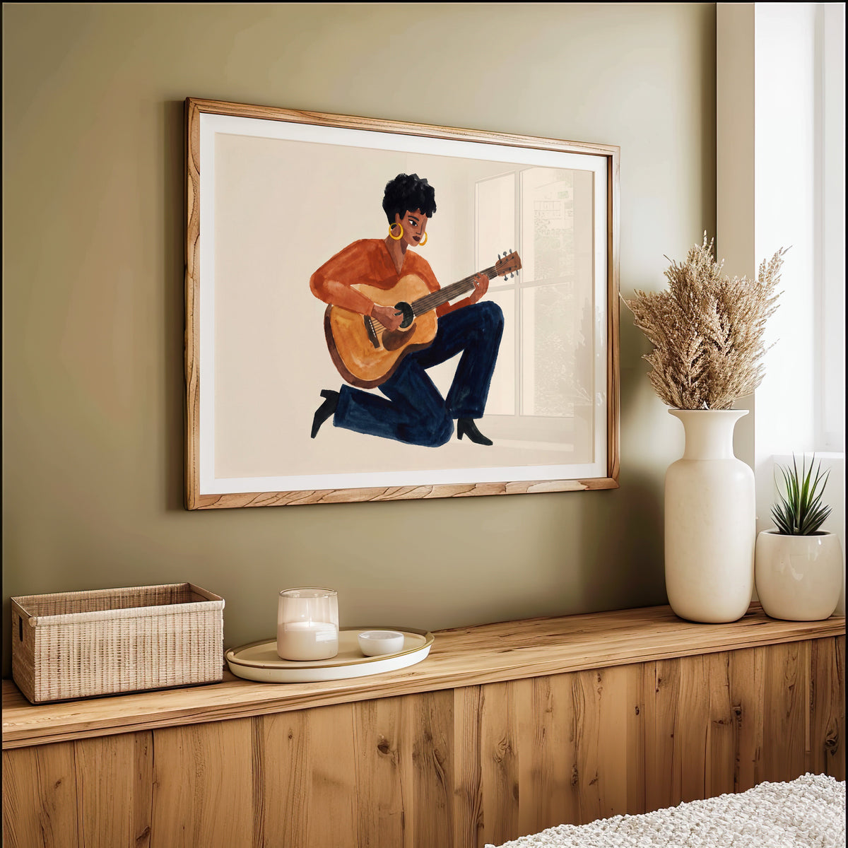Woman playing guitar watercolor print in an oak frame on an olive green wall above pampas grass
