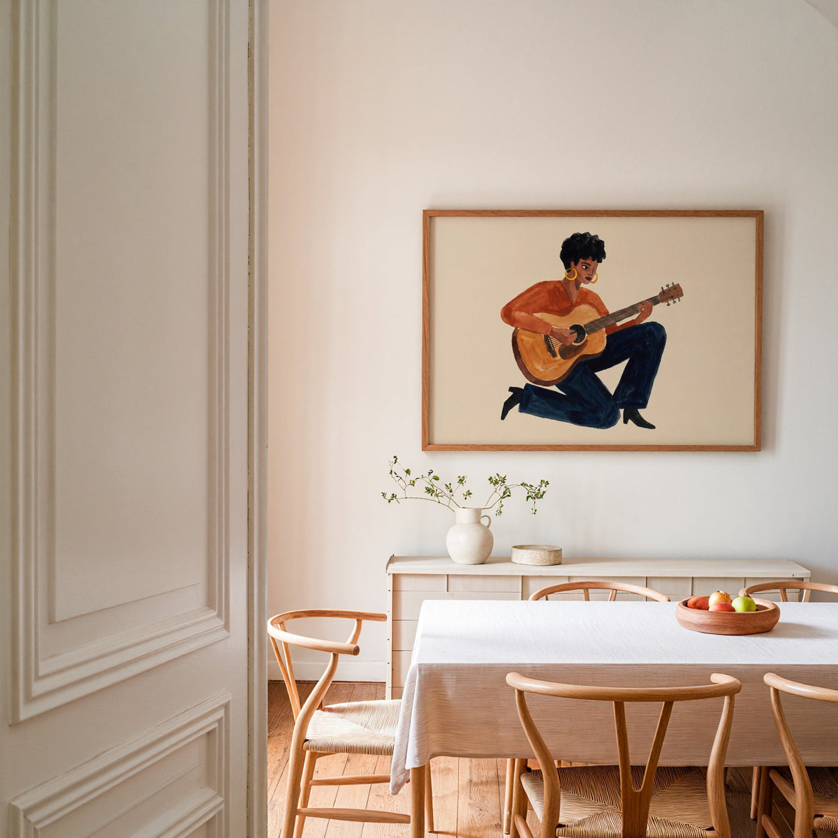 Watercolor guitarist print in an oak frame in a dining room with wishbone chairs