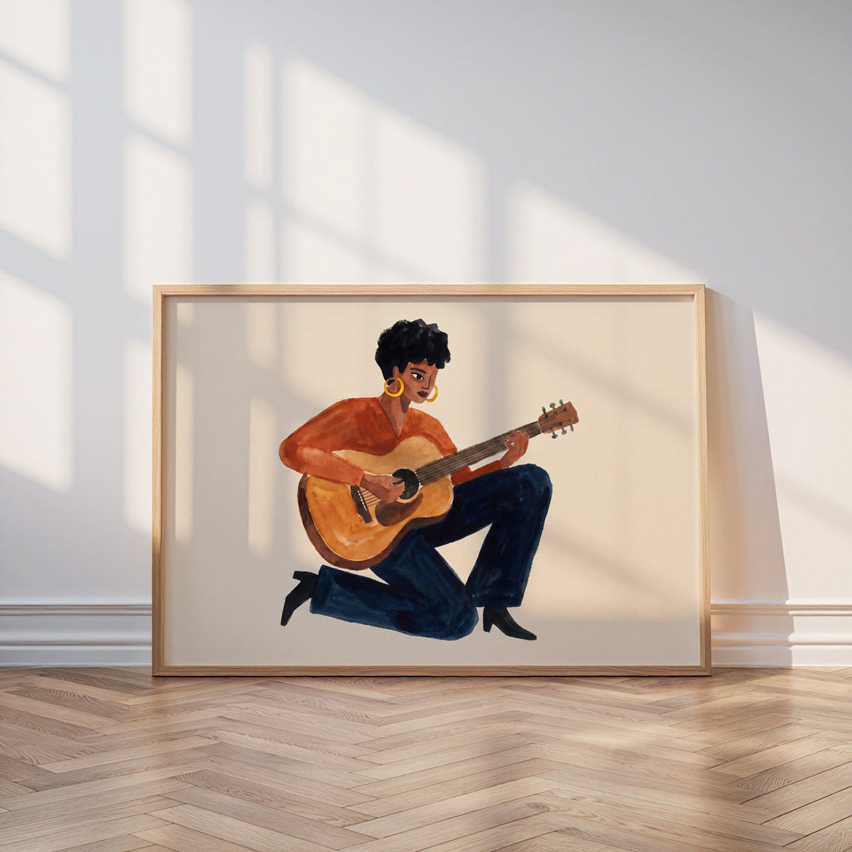 Rust and navy guitar print in an oak frame leaning on a parquet floor in window light