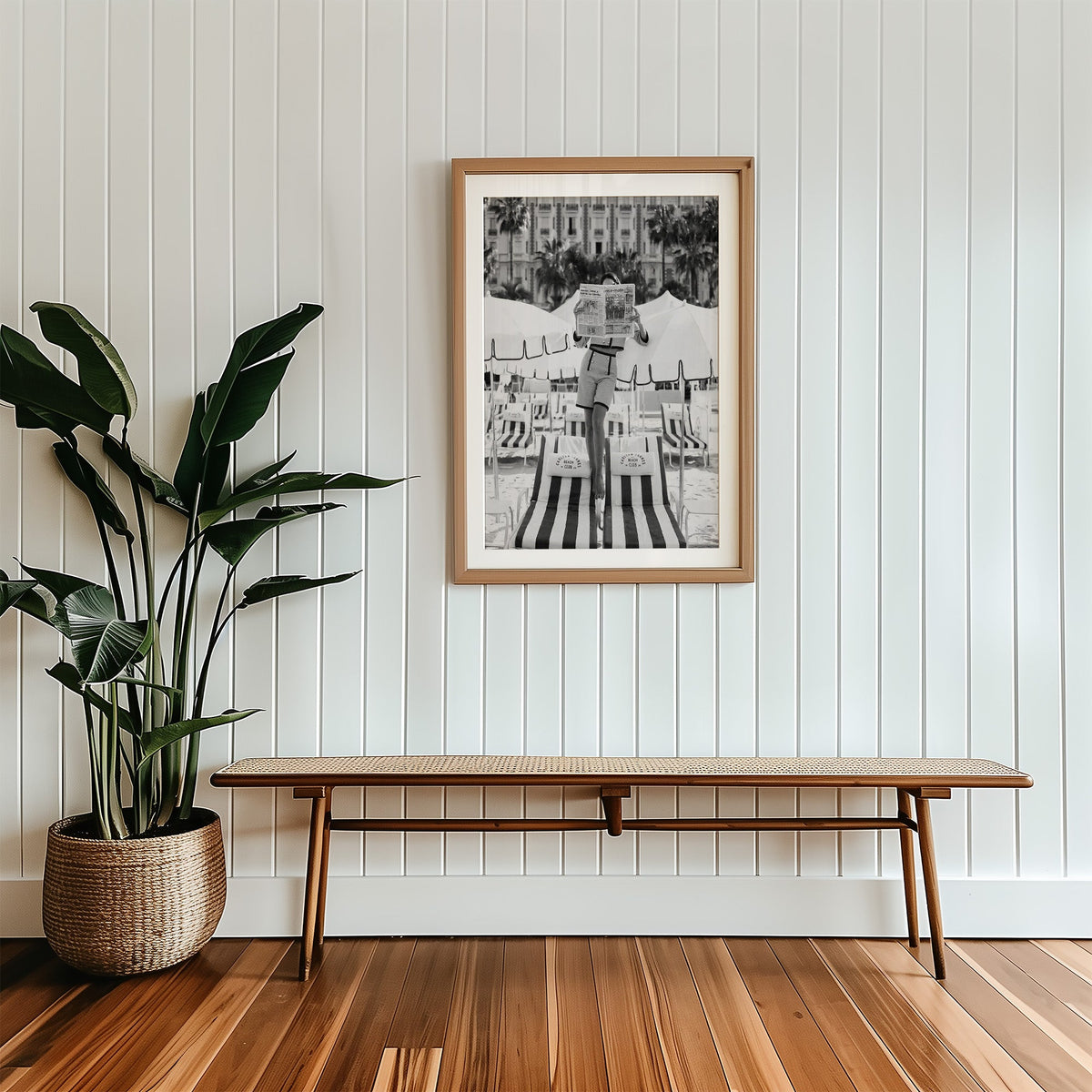 Woman in tweed suit reading a newspaper on a beach print in a wood frame with a white mat above a cane bench