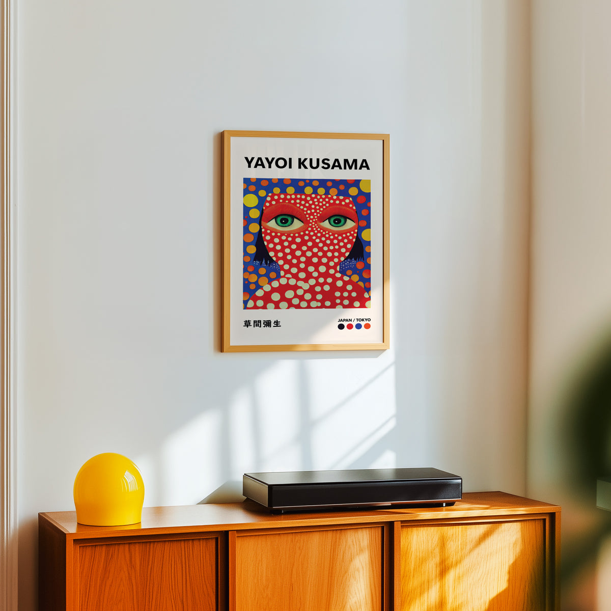 Yayoi Kusama inspired red face green eyes print above a sideboard with a yellow lamp