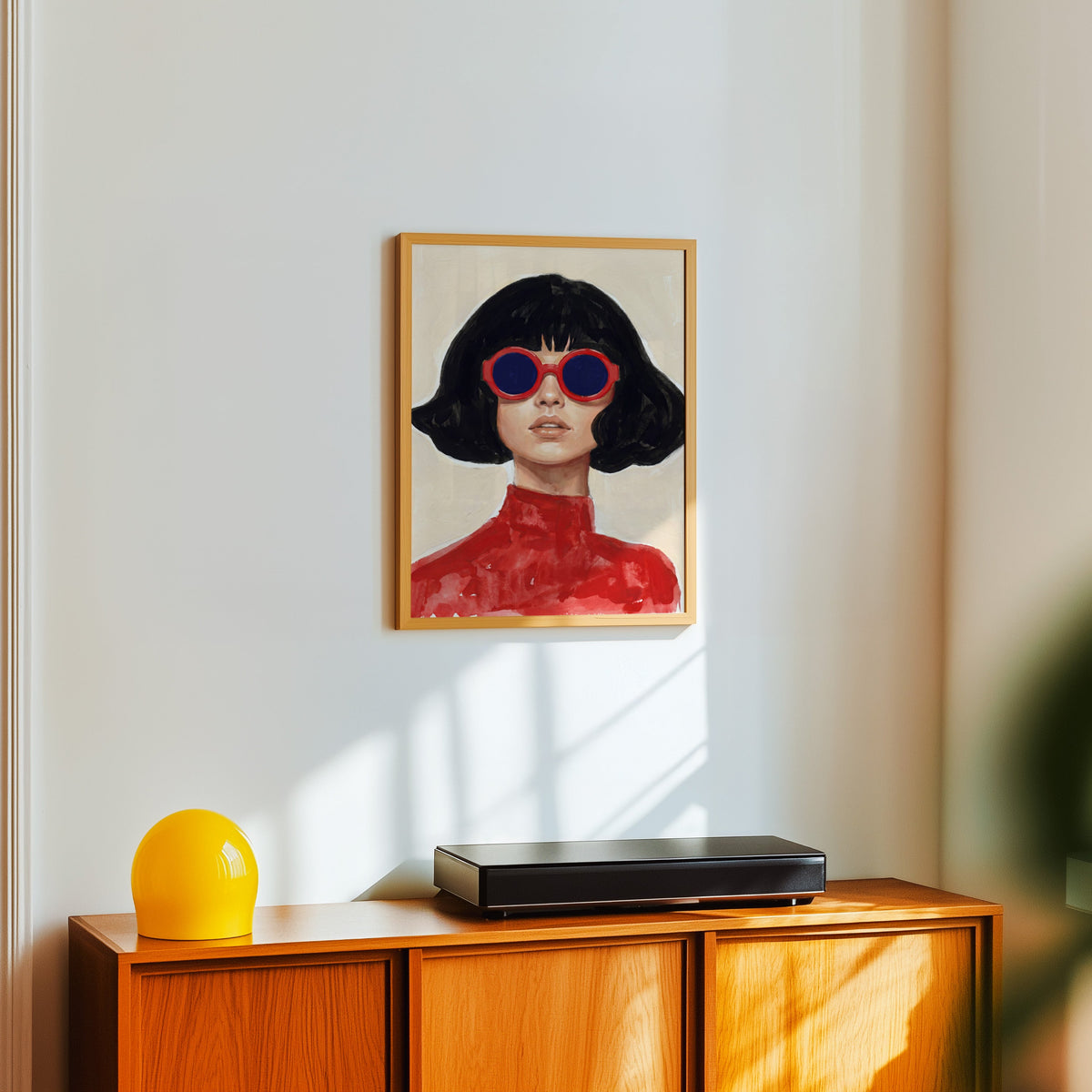 Mod sunglasses portrait print in a light oak frame above a teak sideboard with a yellow lamp