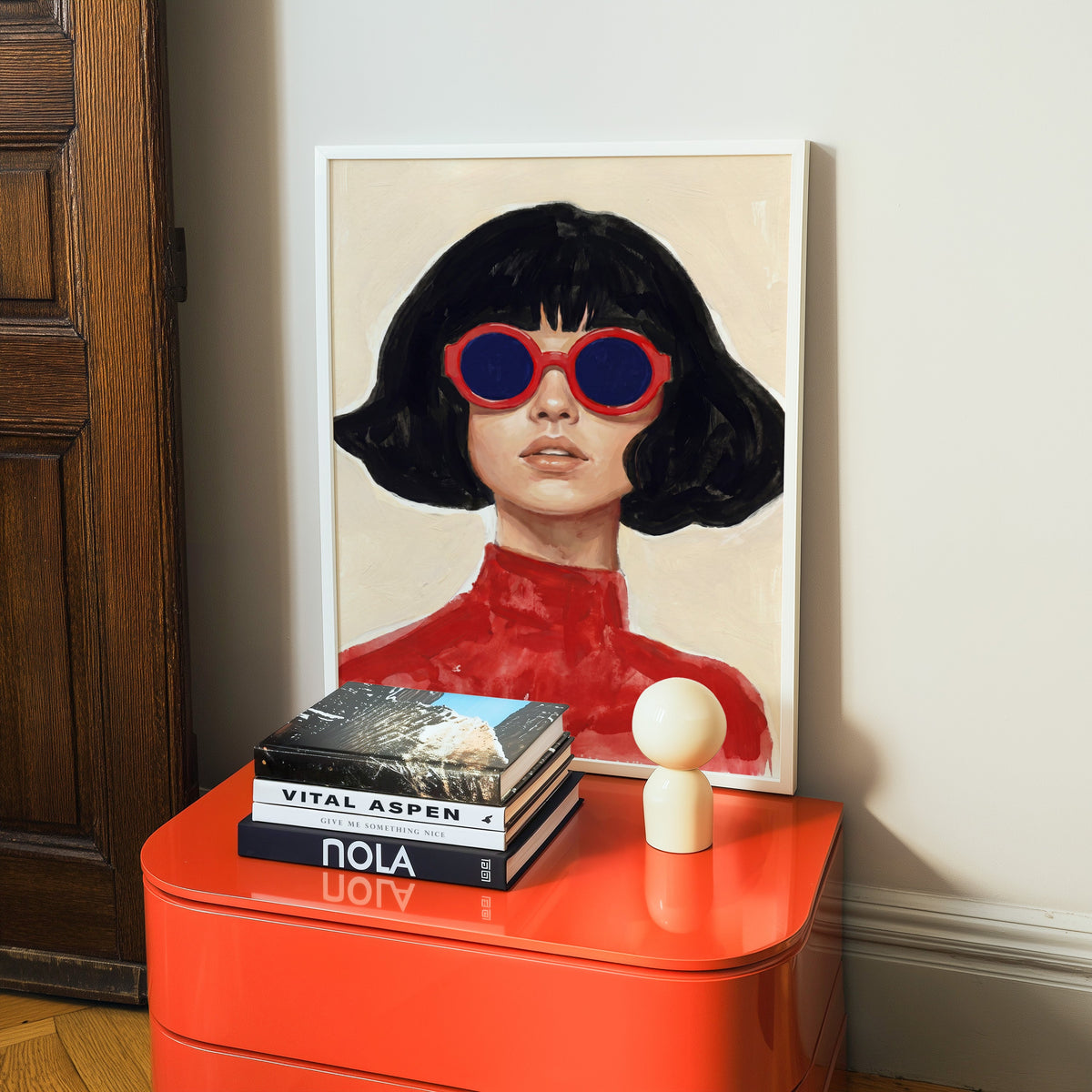 Retro fashion portrait print in a white frame on a glossy orange cabinet with books