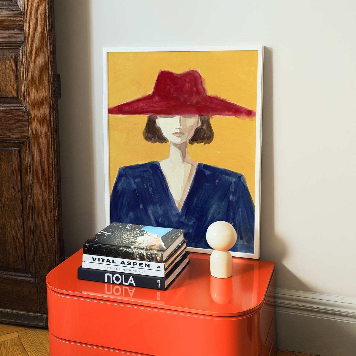 Watercolor fashion portrait print in a white frame on a glossy orange cabinet with books