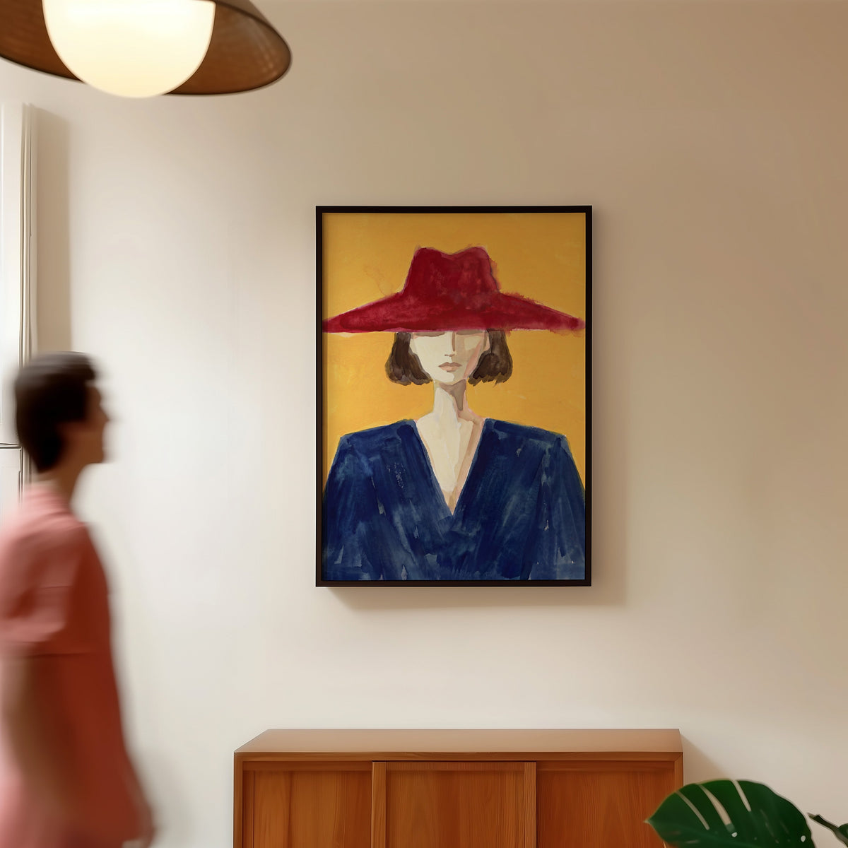 Mustard fashion illustration print in a black frame in a hallway under a rattan pendant