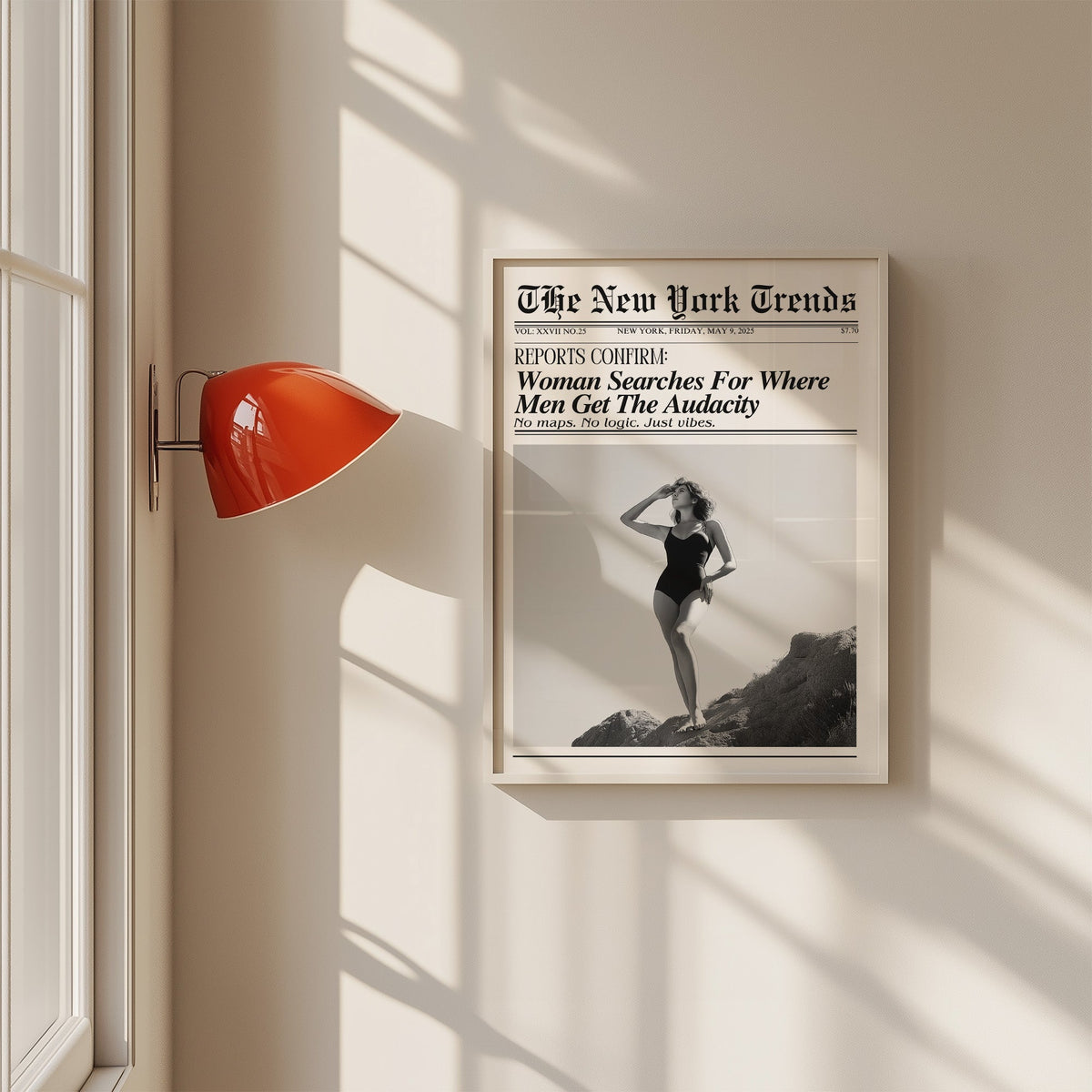 Woman on rocks shading her eyes mock newspaper print in a white frame on a sunlit wall beside a red sconce