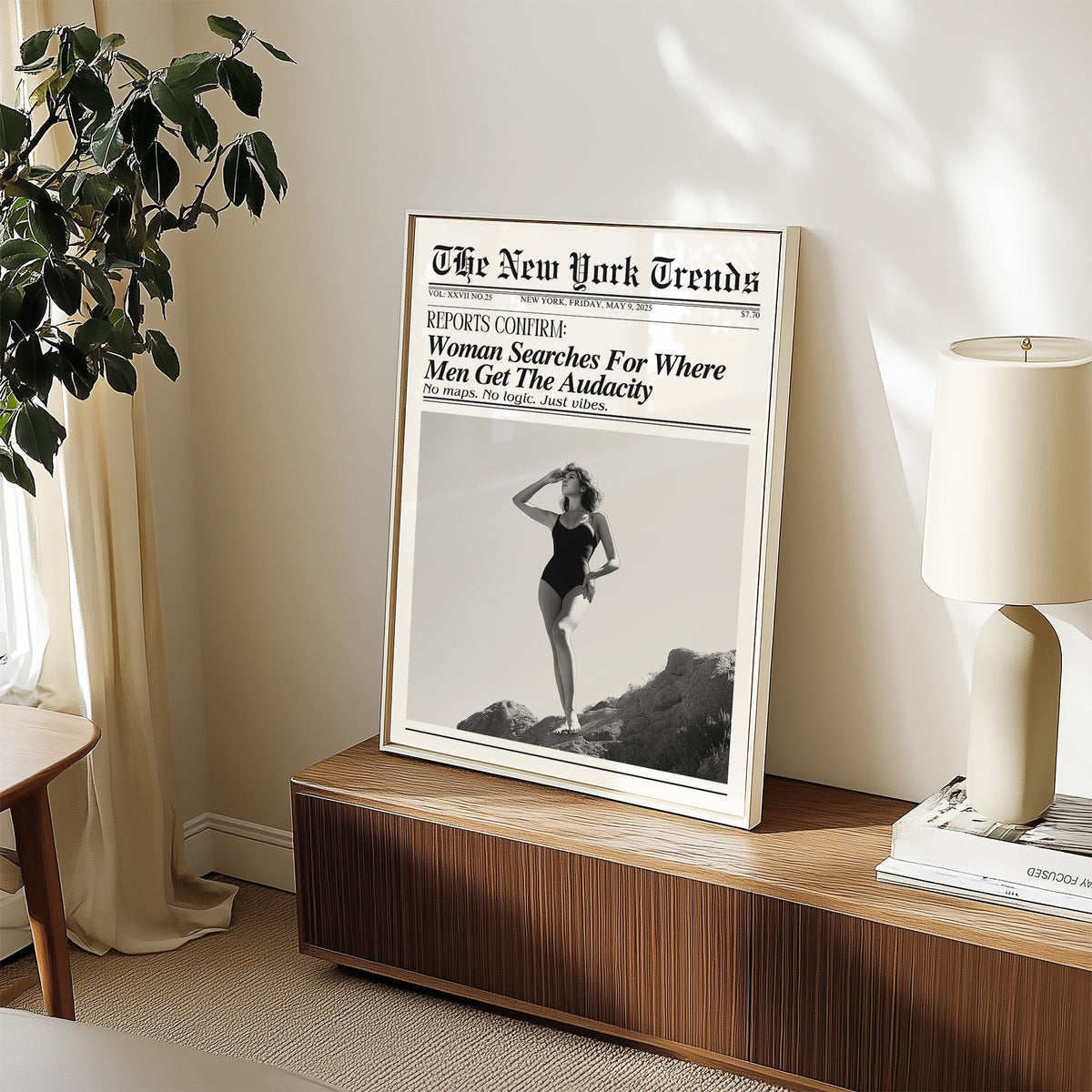 Woman on rocks shading her eyes mock newspaper print in a white frame on a walnut sideboard beside a ceramic lamp