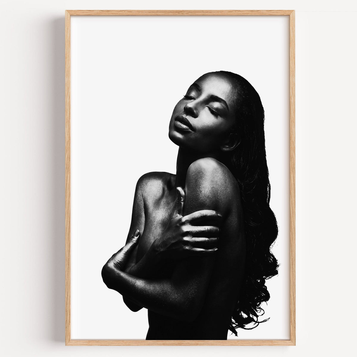 Backlit woman silhouette hugging her shoulders print in a light oak frame on a plain white wall
