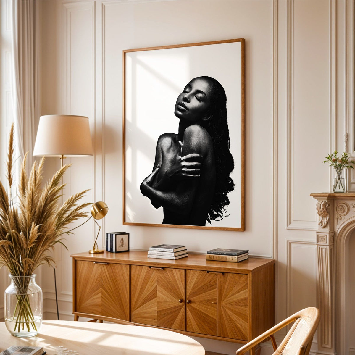 Backlit woman silhouette hugging her shoulders print in an oak frame above a sunburst wood sideboard with pampas grass
