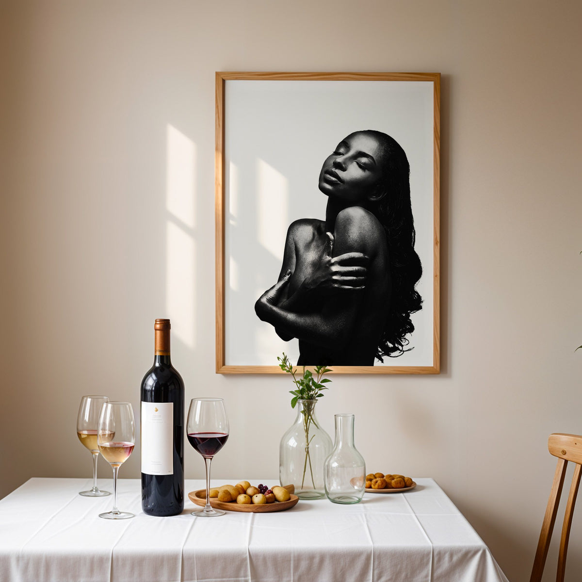 Backlit woman silhouette hugging her shoulders print in an oak frame above a table set with red wine and glasses
