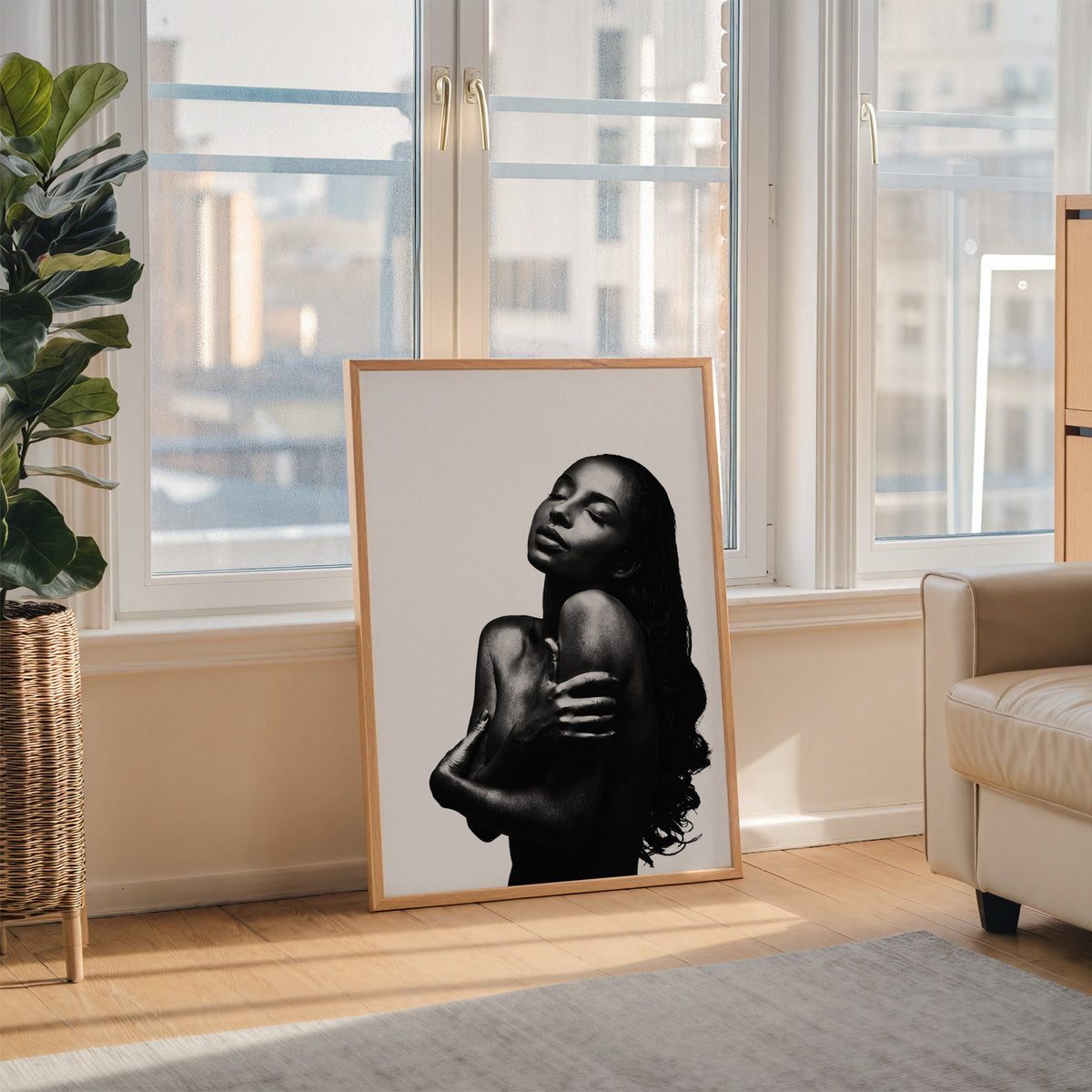 Backlit woman silhouette hugging her shoulders print in an oak frame leaning on the floor beside a fiddle leaf fig