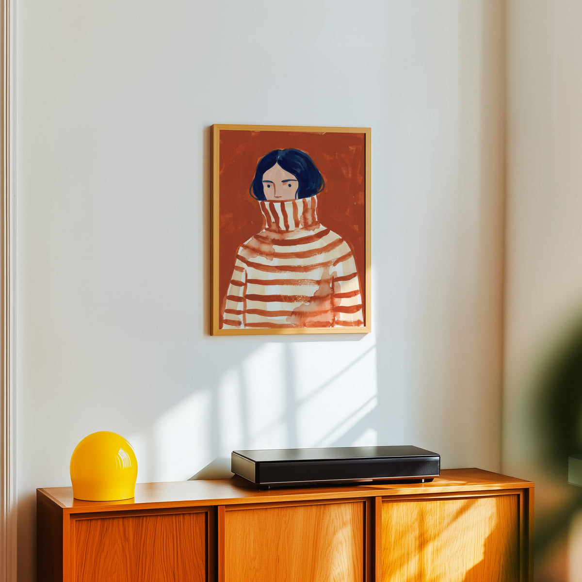 Striped sweater portrait print in a light oak frame above a teak sideboard with a yellow lamp