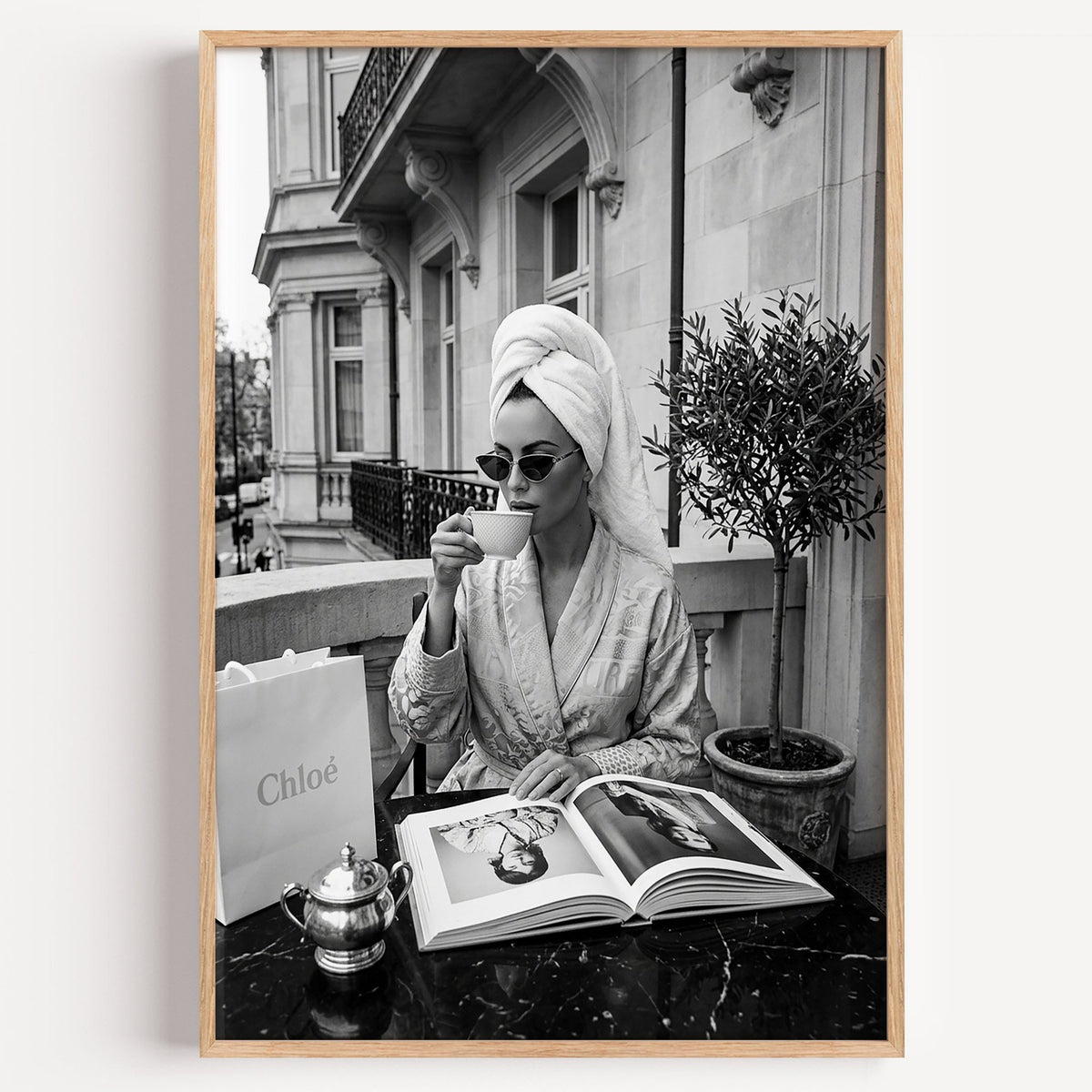 Woman in towel turban drinking coffee on balcony print in a light oak frame on a plain white wall