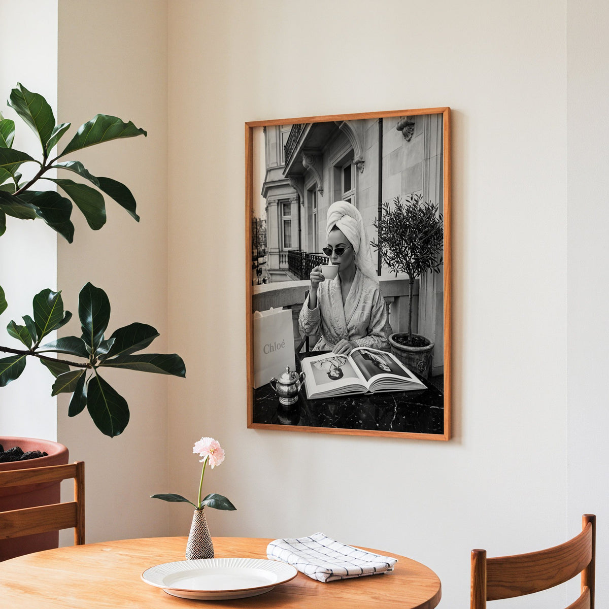 Woman in towel turban drinking coffee on balcony print in a teak frame above a round wooden dining table
