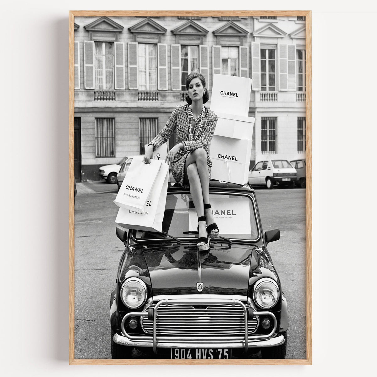 Woman in tweed suit on vintage mini car print in a light oak frame on a plain white wall