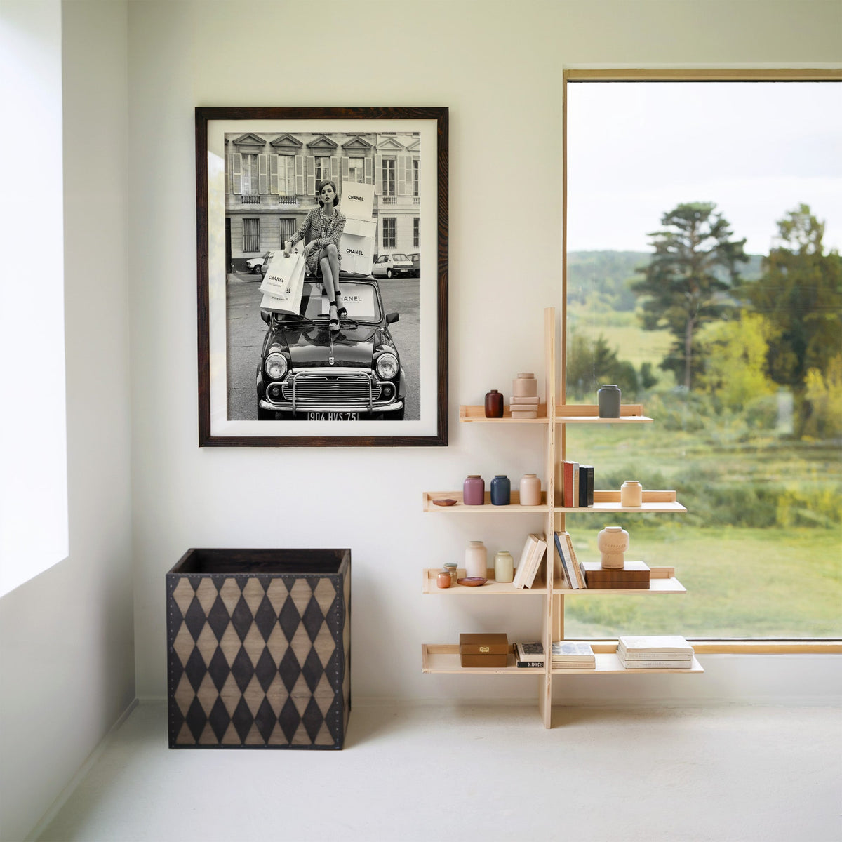 Woman in tweed suit on vintage mini car print in a walnut frame with a white mat beside wooden shelves and a garden window