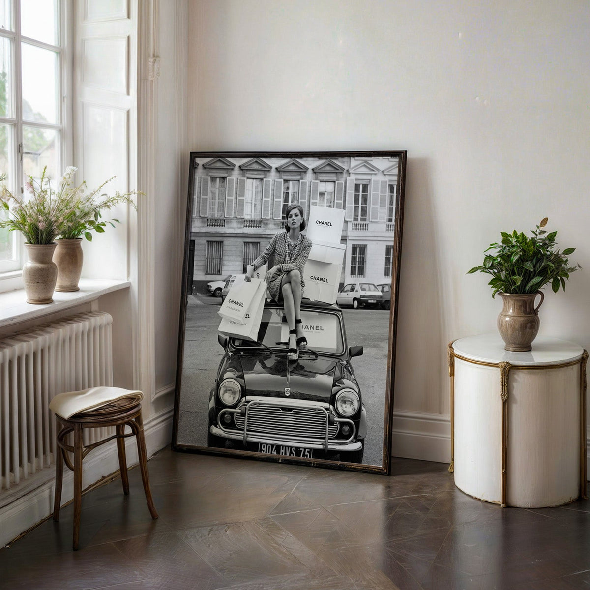 Woman in tweed suit on vintage mini car print in a black frame on a dark stone floor beside a white side table