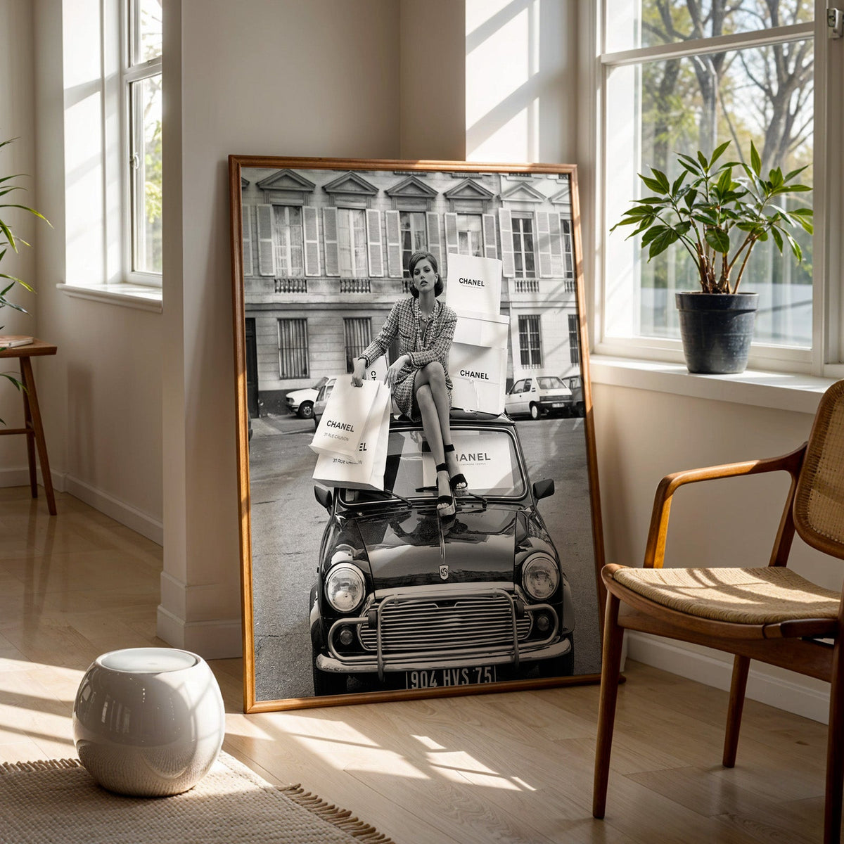Woman in tweed suit on vintage mini car print in a walnut frame on a wood floor beside a cane chair and sunny window